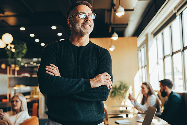 Middle age male with short beard and glasses looking out the window while employees behind work to implement a new plan with a hybrid QDIA.